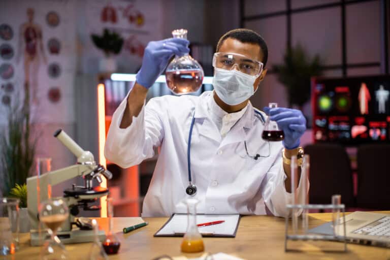 Experienced male scientist in protective mask and goggles doing analysis of substance